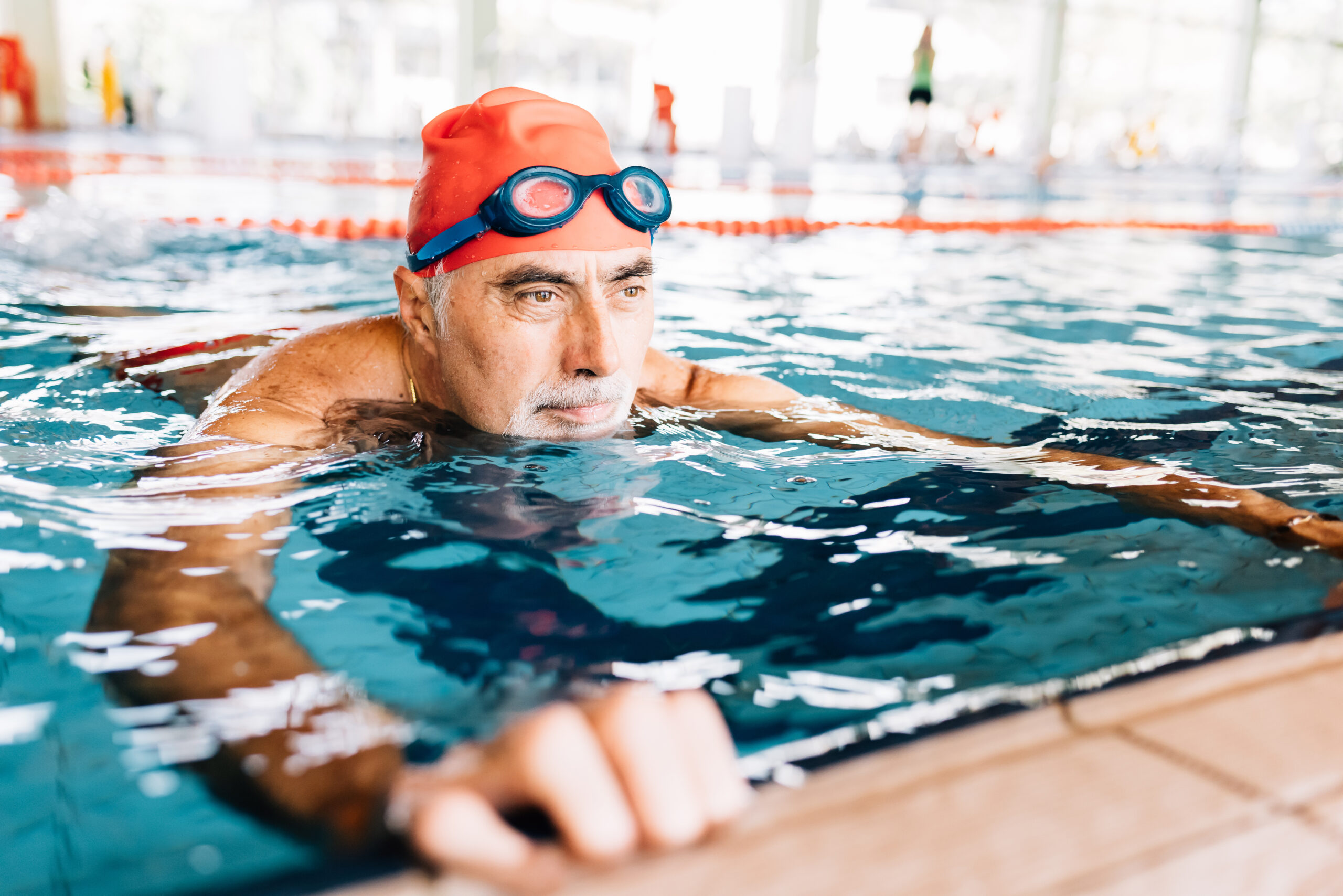Senior man relaxing in water by edge of swimming pool